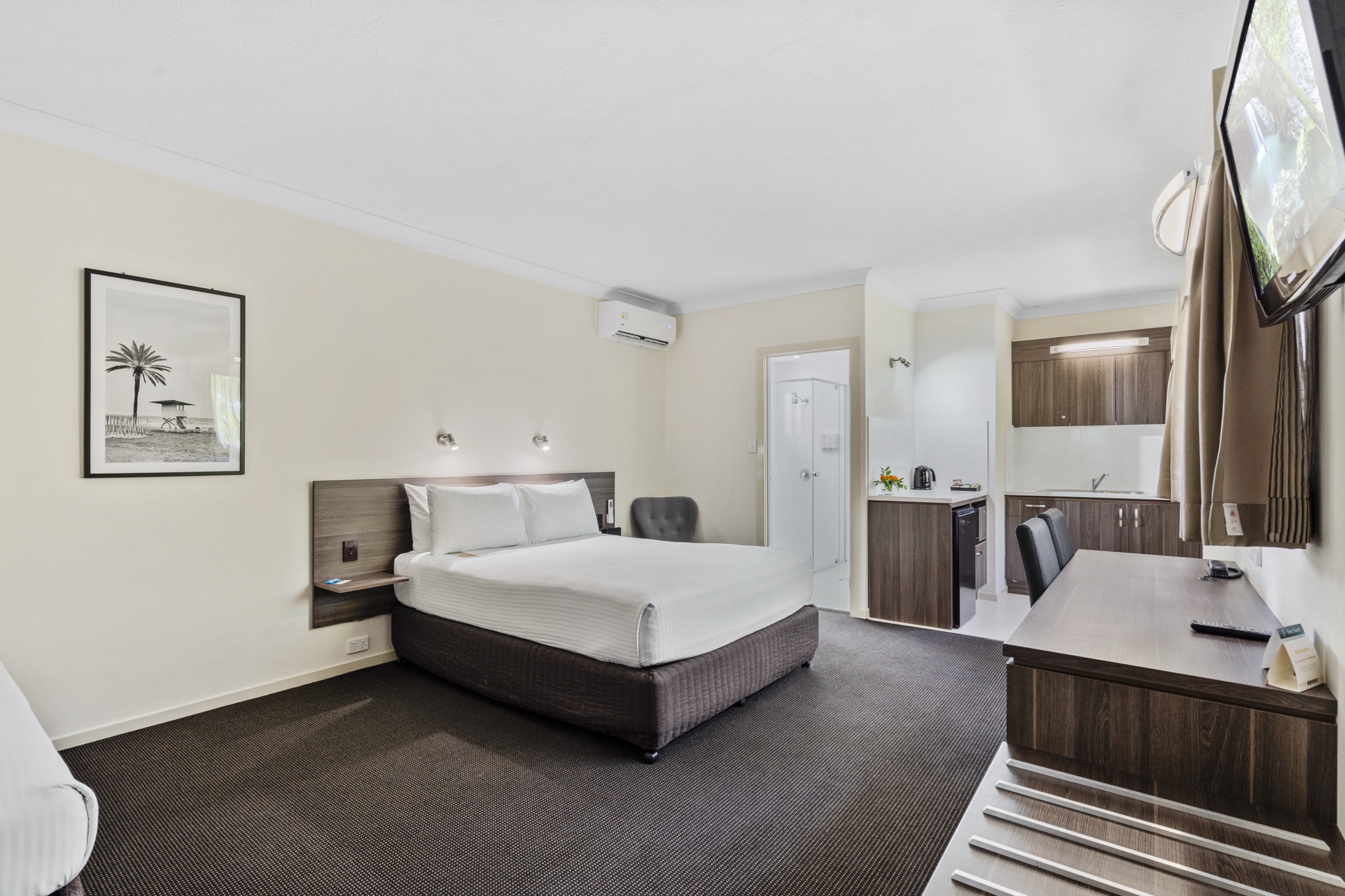 A guest room with a queen bed, work desk and garden artwork